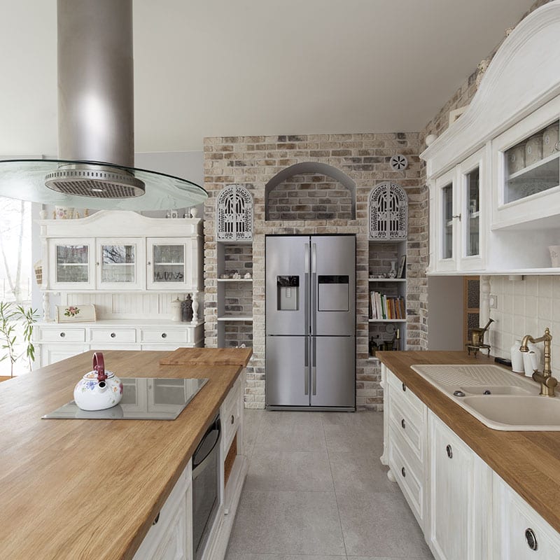 Remodeled kitchen with white painted cabinetry, butcher-block countertops and an exposed brick wall