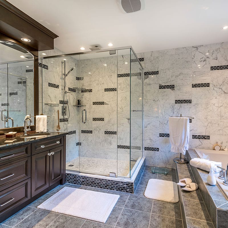 Renovated bathroom with a frameless glass shower, marble tile surround and dark wood vanity
